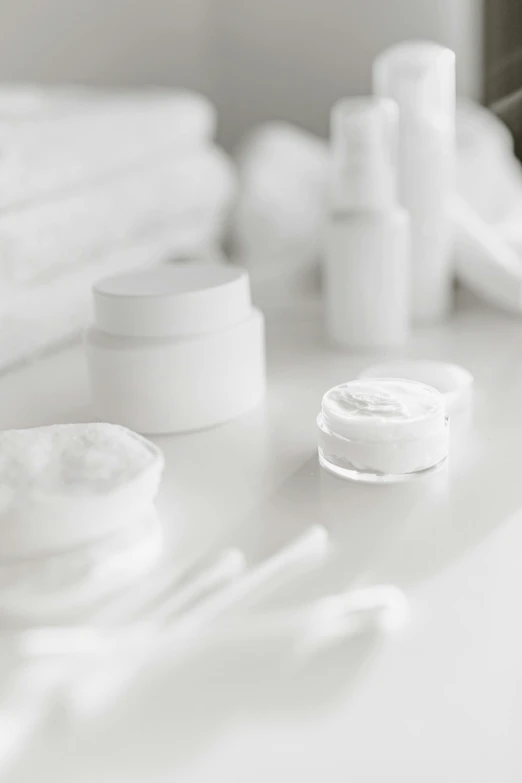 a table topped with lots of different types of skin care products, a black and white photo, trending on pexels, plasticien, wearing white clothes, in white room, white mechanical details, white petal