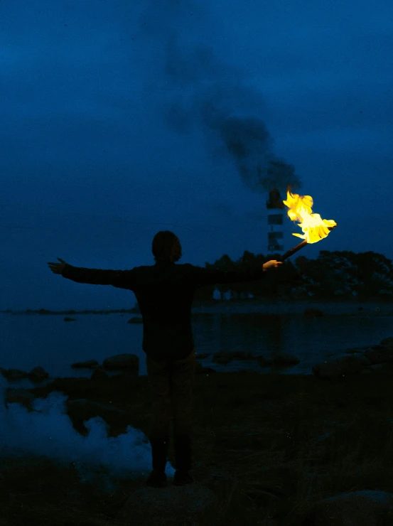 a man standing on top of a beach next to a body of water, an album cover, inspired by Scarlett Hooft Graafland, unsplash, environmental art, holding a torch, lights with bloom, fuming effigy, profile image