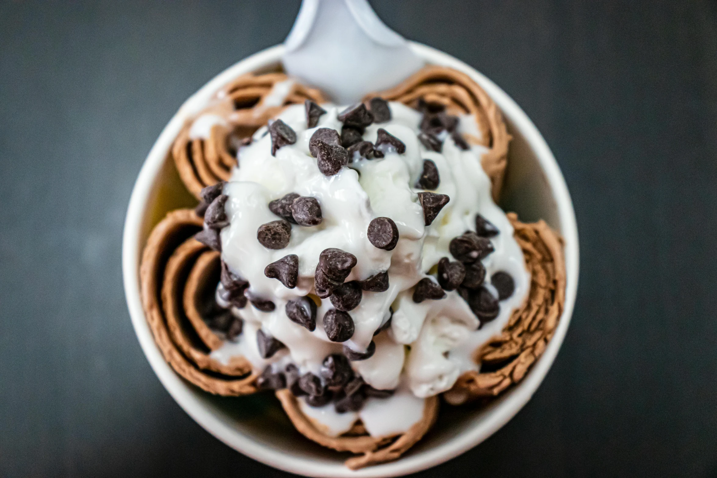 a bowl of ice cream topped with chocolate chips, windings, chocolate river, yogurt, whip