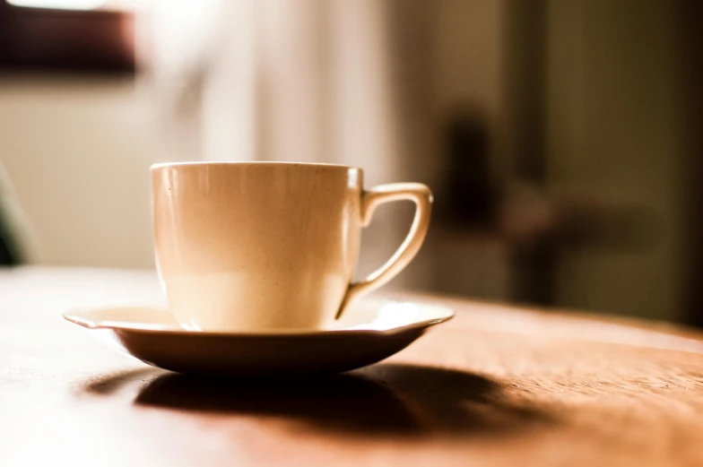 a coffee cup sitting on top of a wooden table, unsplash, renaissance, medium format. soft light, ivory, single light, awkward