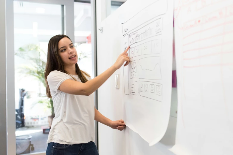 a woman writing on a white board in an office, a wireframe diagram, pexels contest winner, 9 9 designs, in australia, programming, model pose