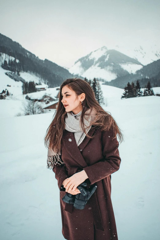 a woman standing in the snow with mountains in the background, pexels contest winner, attractive brown hair woman, brown clothes, instagram post, slightly pixelated