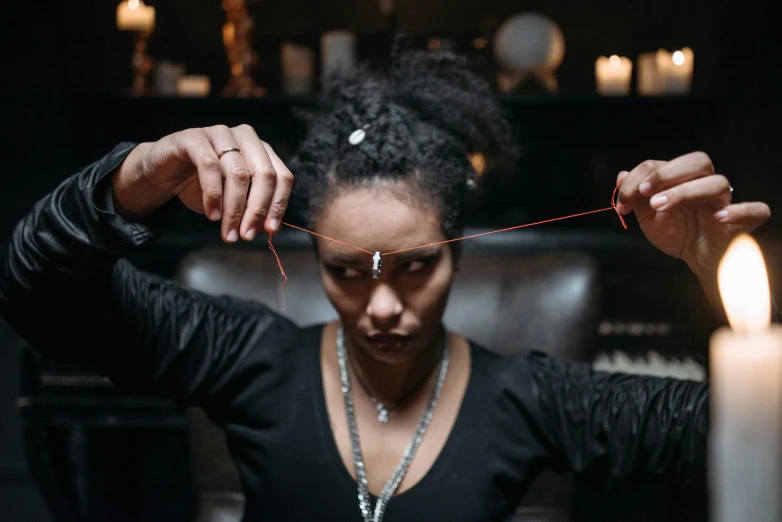 a woman lighting a candle in a dark room, a portrait, by Emma Andijewska, kinetic art, short dreadlocks with beads, pulling strings, gemstone forehead, thumbnail