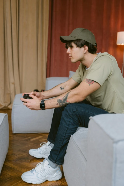 a man sitting on a couch playing a video game, by Adam Marczyński, trending on pexels, hyperrealism, jamie campbell bower, wearing a baseball hat, declan mckenna, confident looking