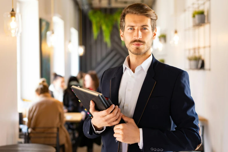 a man in a suit holding a tablet computer, a portrait, by Niko Henrichon, pexels contest winner, standing in a restaurant, librarian, attractive male, lachlan bailey