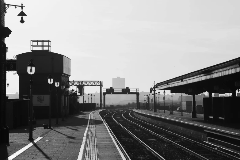 a black and white photo of a train station, by Ian Fairweather, pexels, clear skies in the distance, beautifully daylight, cityscape, platforms