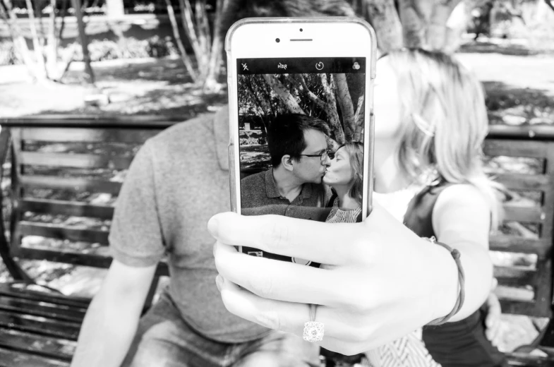 a black and white photo of a man and a woman on a bench, a black and white photo, pexels, realism, hold up smartphone, kiss, mirror selfie, color splash