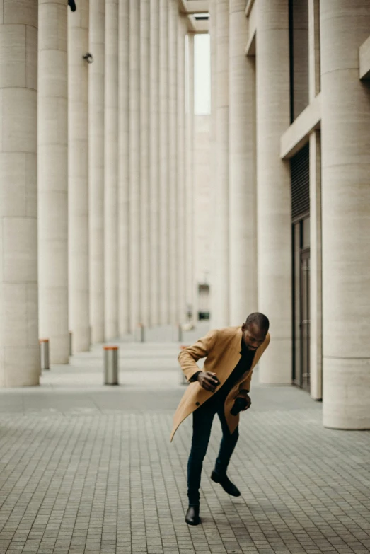 a man that is standing in the middle of a walkway, brown clothes, checking her phone, golden pillars, brutalist appearance