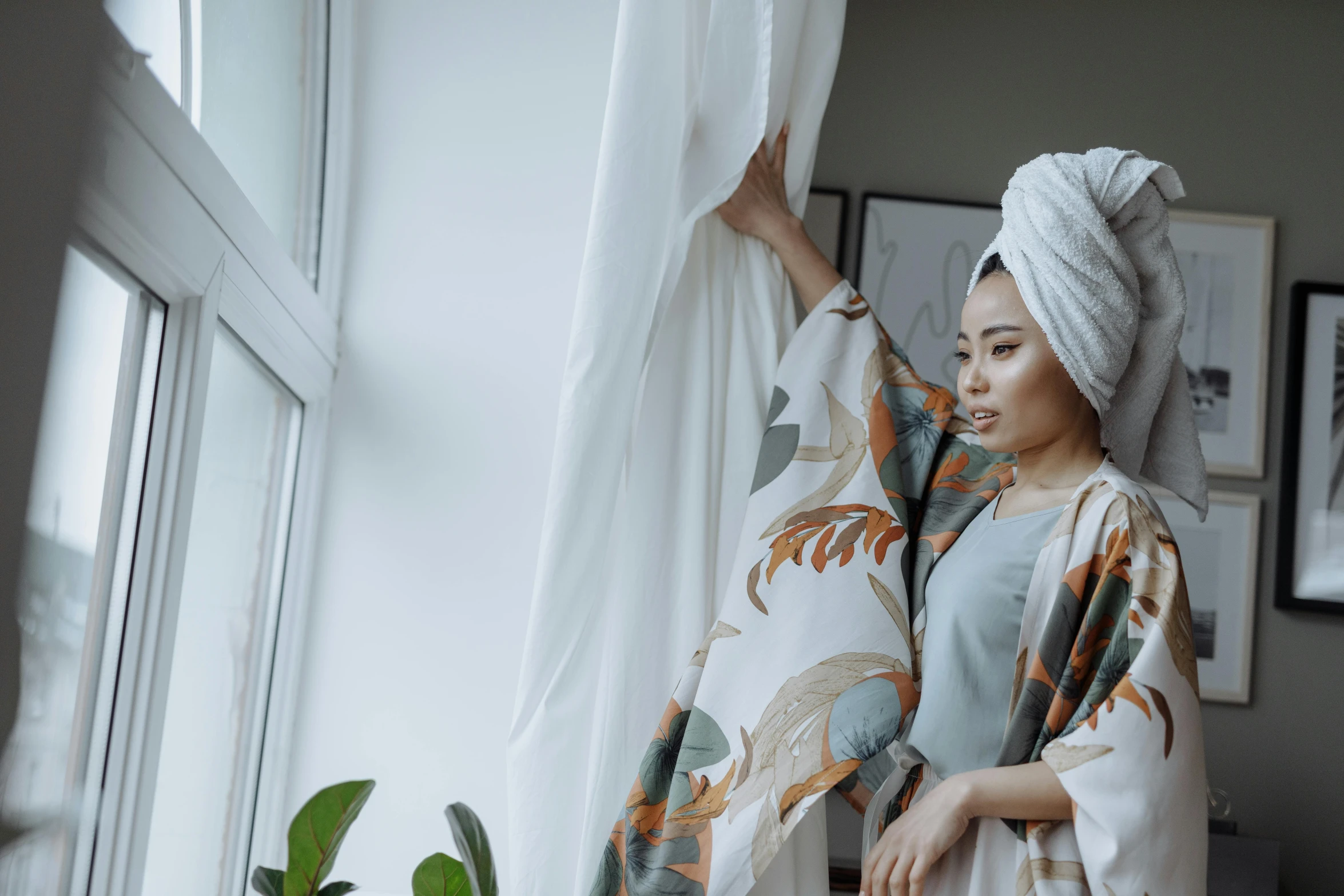 a woman standing next to a window with a towel on her head, inspired by Ruth Jên, pexels contest winner, arabesque, wearing pajamas, asian woman, fully covered in drapes, angle view
