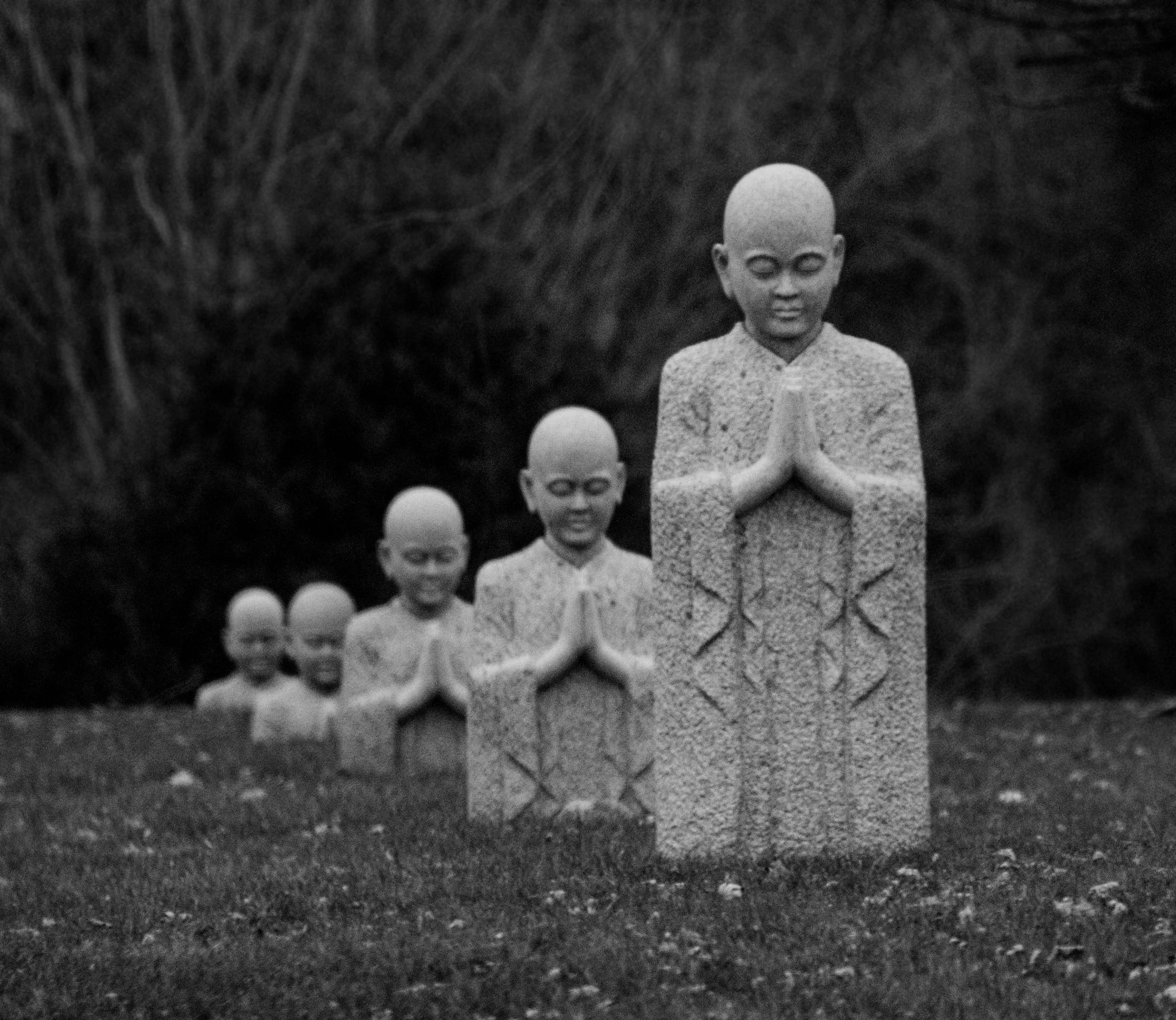 a group of statues sitting on top of a grass covered field, inspired by Antanas Sutkus, flickr, concrete art, taoist priest, haunting!, buddhist art, grey porcelain sculpture