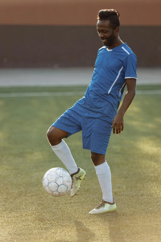 a man kicking a soccer ball on a field, trending on dribble, blue uniform, ( ( dark skin ) ), compression, contemplating