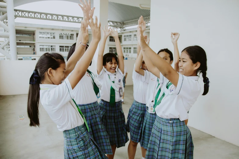 a group of young girls standing next to each other, pexels contest winner, happening, white shirt and green skirt, arms raised, philippines, in school hallway