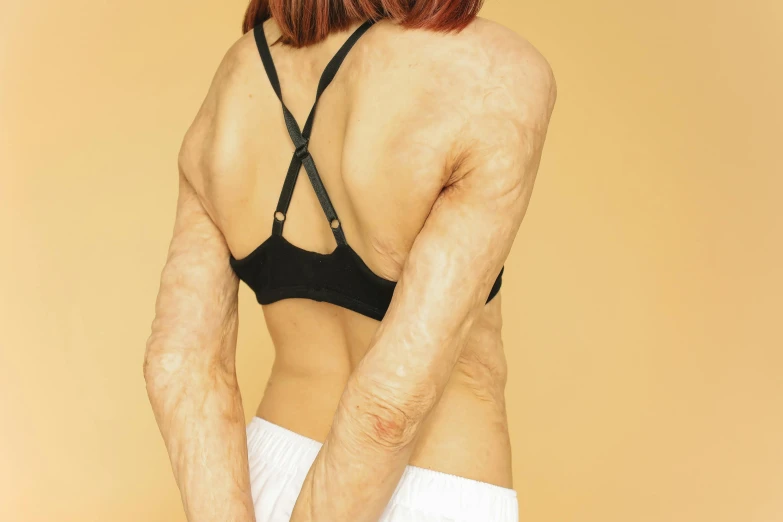 a woman in a black bra top holding a tennis racquet, inspired by Vanessa Beecroft, figuration libre, wrinkled muscles skin, prosthetic makeup, with damaged rusty arms, from the back