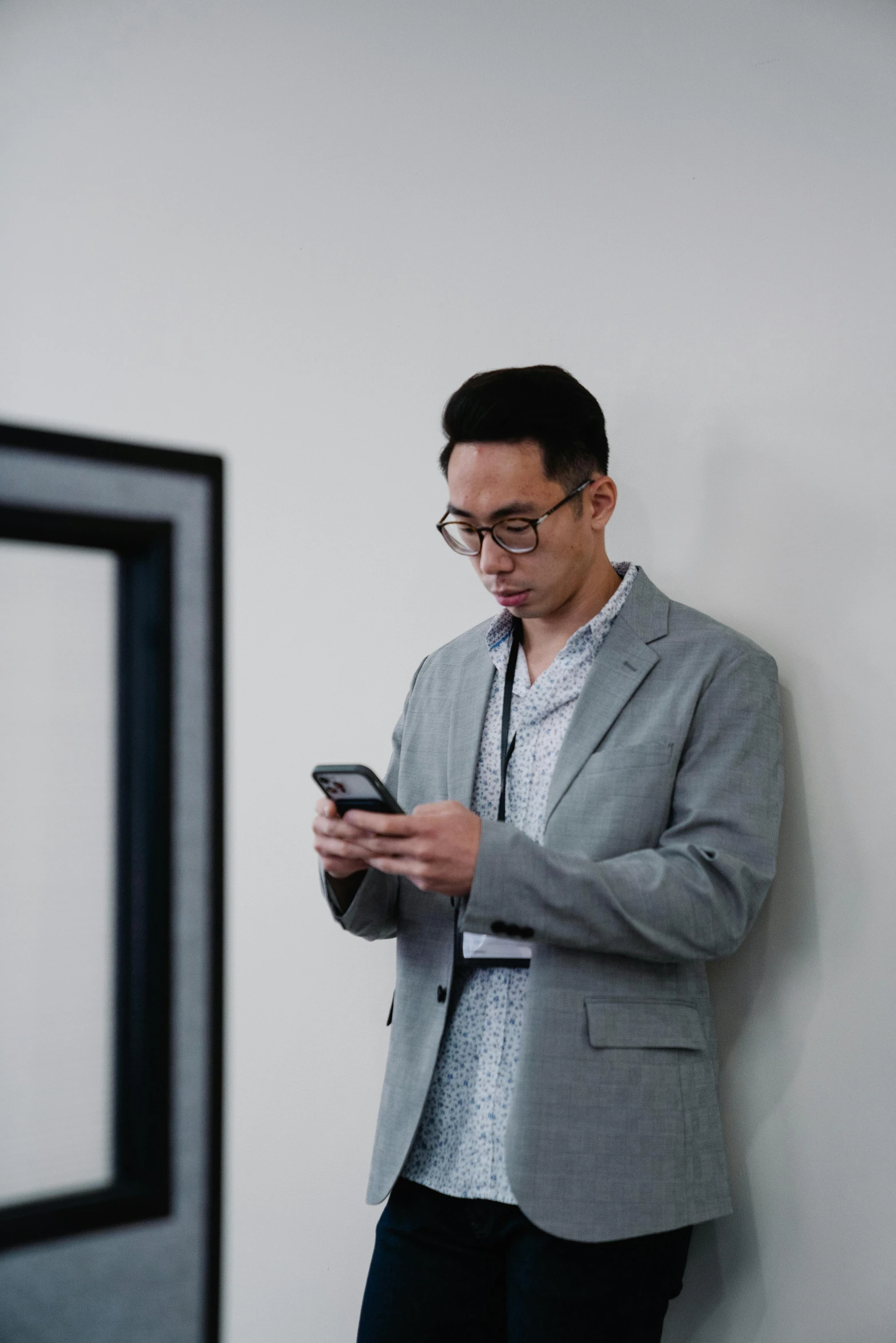 a man leaning against a wall using a cell phone, by Robbie Trevino, in a museum room, wearing a suit and glasses, damien tran, mobile learning app prototype