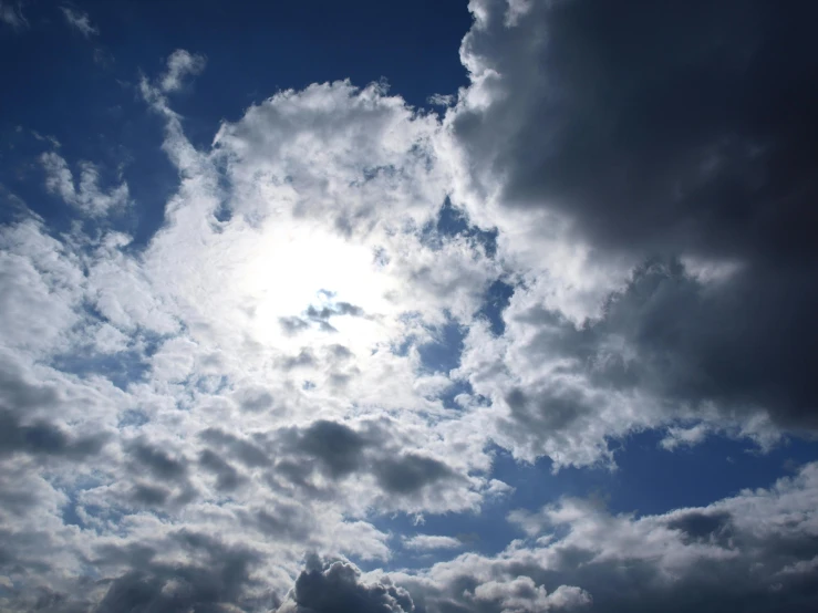 a person flying a kite under a cloudy sky, sun overhead, layered stratocumulus clouds, looking up onto the sky, dark blue sky