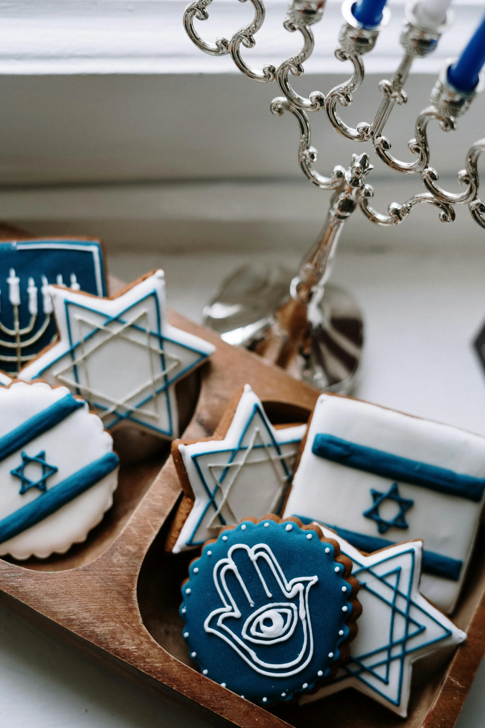 a wooden tray topped with cookies next to a candelab, by Julia Pishtar, beautiful jewish woman, white and blue, holy themed, full product shot