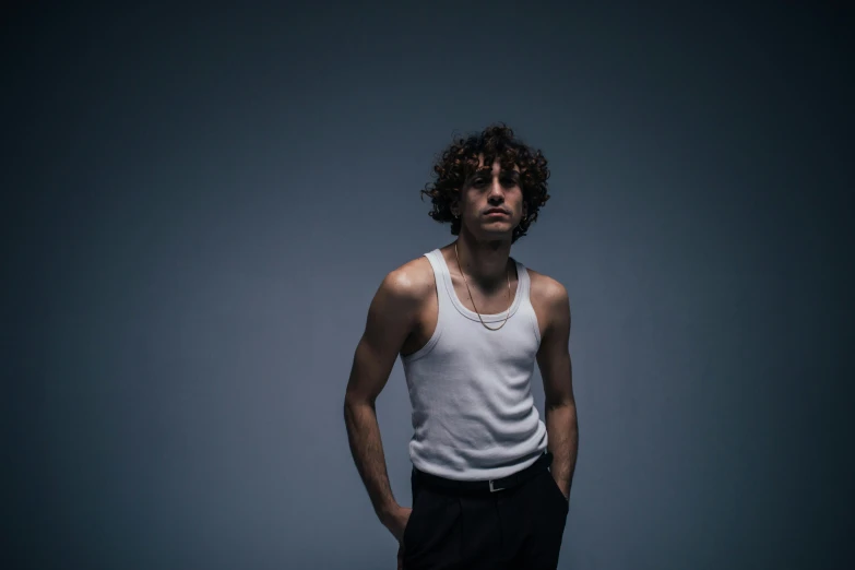 a man standing with his hands in his pockets, an album cover, by Jacob Toorenvliet, trending on pexels, photorealism, robert sheehan, in a white tank top singing, dramatic lowkey studio lighting, promotional image