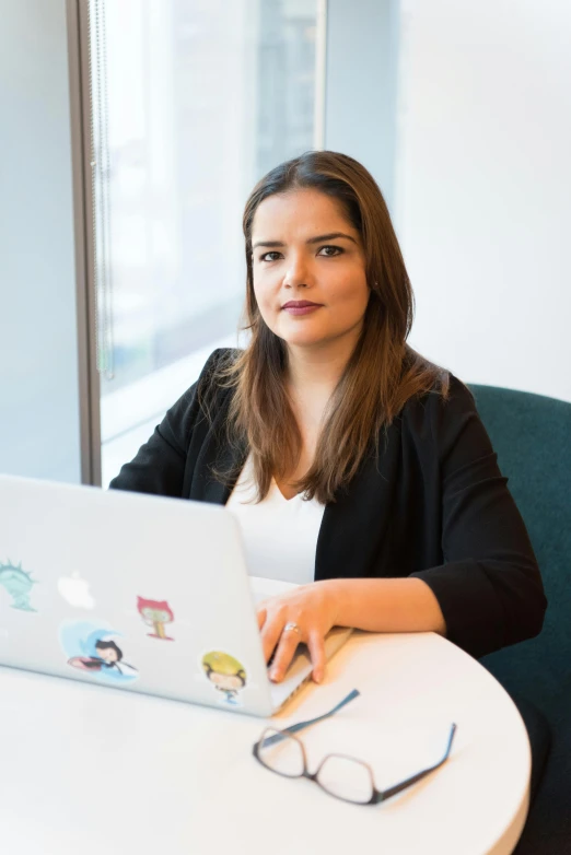 a woman sitting at a table with a laptop, by Alejandro Obregón, trending on reddit, wearing business casual dress, looking towards camera, faridah malik, slightly pixelated