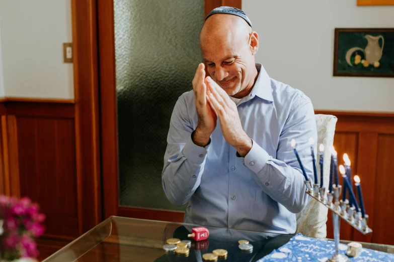 a man in a blue shirt sitting at a table, blessing hands, mutahar laughing, his head covered in jewels, israel