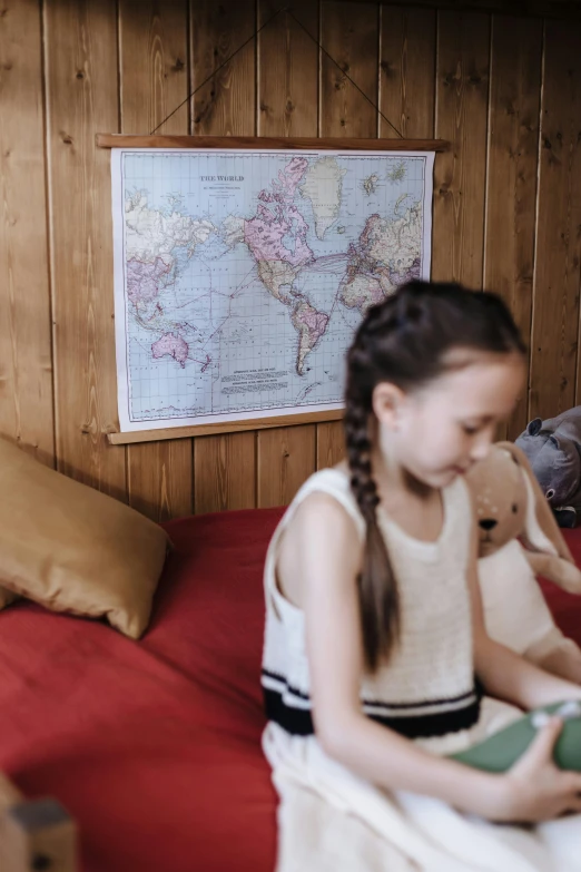 a little girl sitting on a bed holding a teddy bear, a portrait, pexels, cartography map art, in a cabin, world map, 64x64