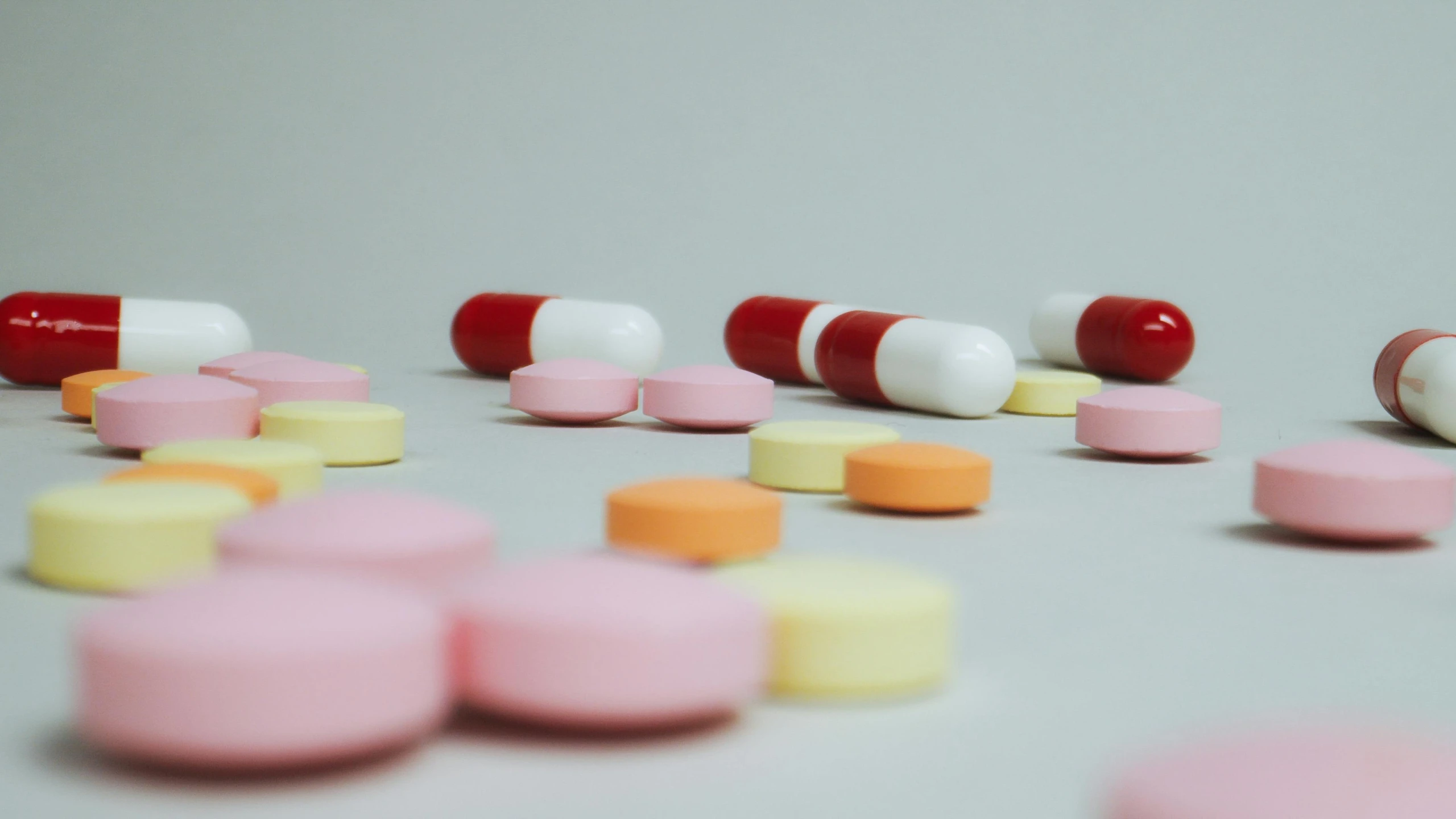 a bunch of pills sitting on top of a table, by Emma Andijewska, pexels, hyperrealism, on grey background, pink and red colors, lined up horizontally, over the shoulder