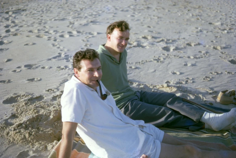 a couple of men sitting on top of a sandy beach, early 2 0 0 0 s, portrait image