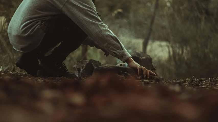 a man crouches down to pick up a dead animal, an album cover, inspired by Elsa Bleda, pexels contest winner, australian tonalism, forestry, worksafe. cinematic, rocks coming out of the ground, gardening