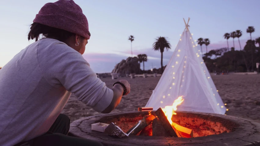 a person sitting in front of a fire pit, pexels contest winner, santa monica beach, teepee, nightcap, on the ocean