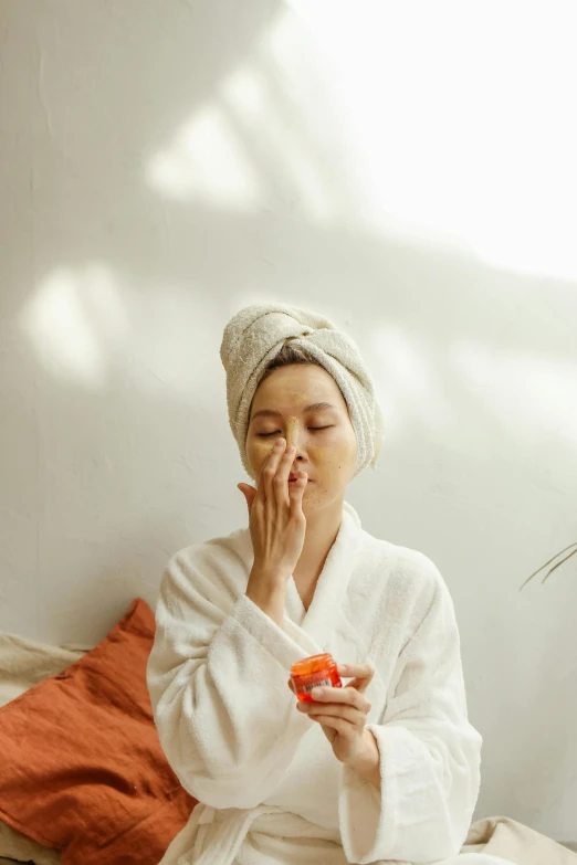 a woman sitting on a bed with a towel on her head, a picture, trending on pexels, drinking cough syrup, flowers covering eyes, asian sun, robe. perfect faces