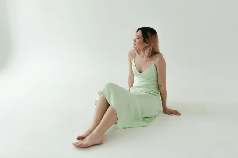 a woman sitting on the floor in a green dress, inspired by Fei Danxu, trending on pexels, realism, pale pastel colours, gradient pastel green, smooth porcelain skin, wearing a camisole