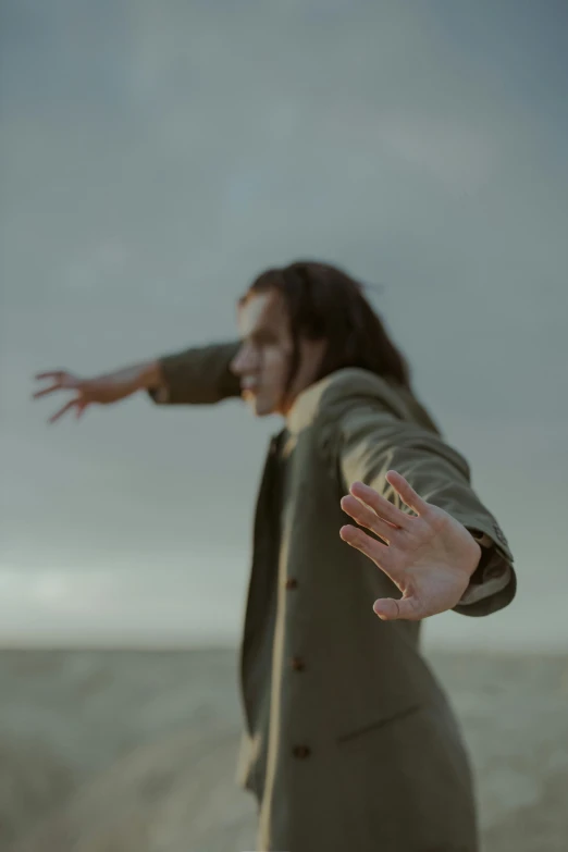 a woman standing on top of a sandy beach, an album cover, by Eglon van der Neer, unsplash, surrealism, severus snape dances in a bar, hand gesture, movie still of a snarling, overcast! cinematic focus