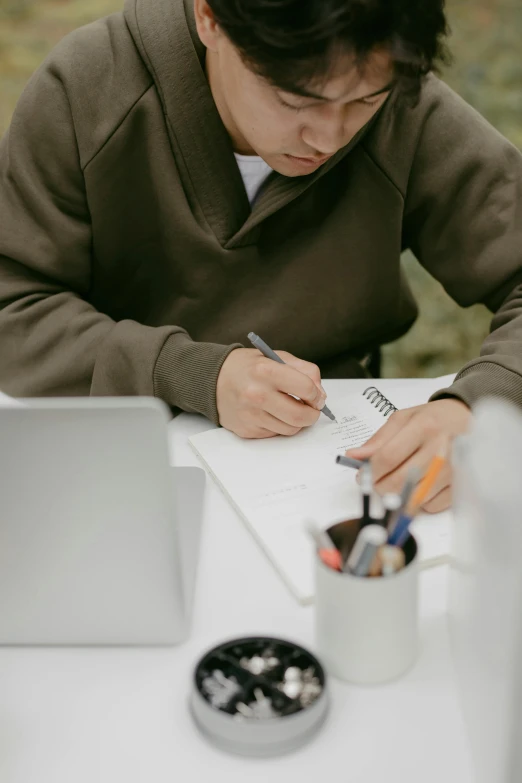 a man sitting at a table writing on a piece of paper, studious, rounded lines, during the day, intense line work