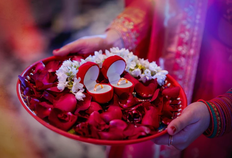 a close up of a person holding a bowl of flowers, red adornments, ring lighting, ceremony, red shoes