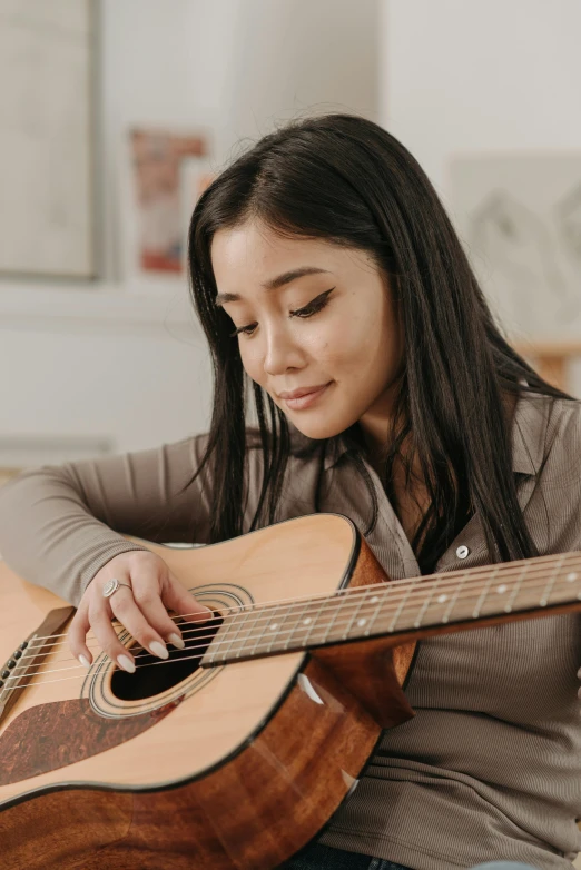 a woman sitting on a couch playing a guitar, inspired by Li Song, trending on pexels, half asian, on grey background, compassionate, instagram picture
