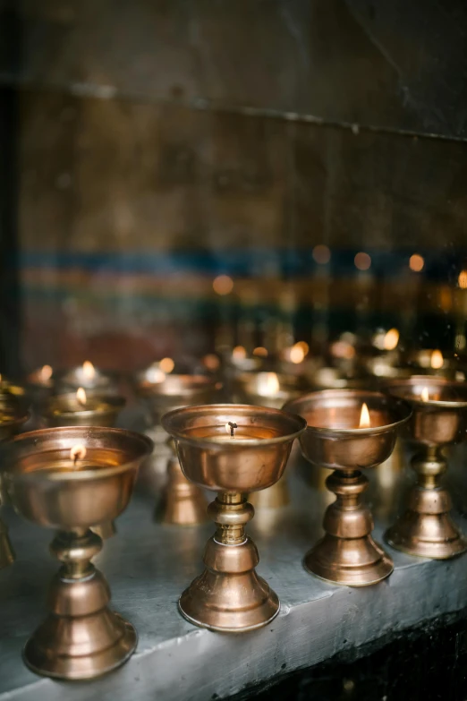 a group of candles sitting on top of a table, in a temple, copper cup, in a monestry natural lighting, sconces