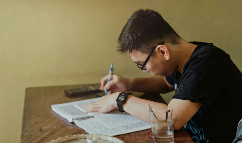 a man sitting at a table writing on a piece of paper, by Robbie Trevino, pexels contest winner, academic art, asian male, background image