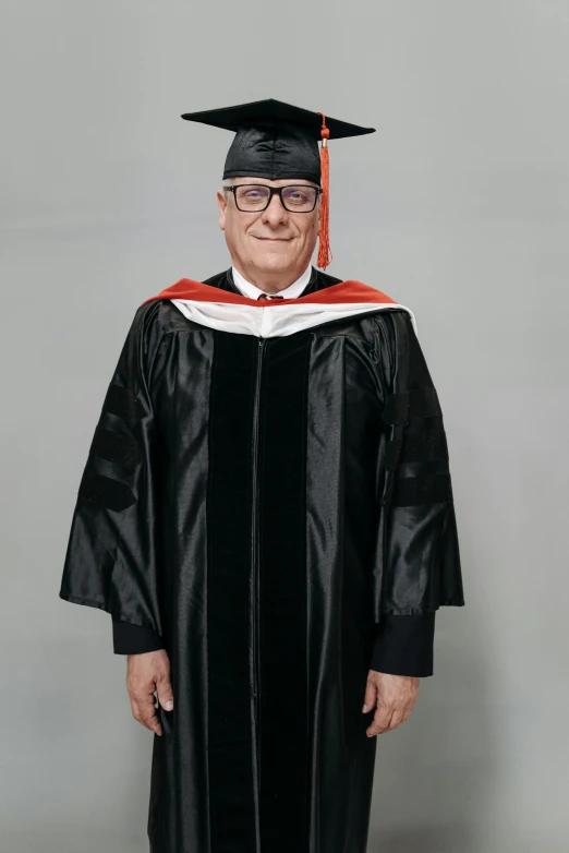 a man in a graduation gown posing for a picture, a colorized photo, by Bernie D’Andrea, reddit, klaus schwab, on grey background, danny devito, he wears dark visors