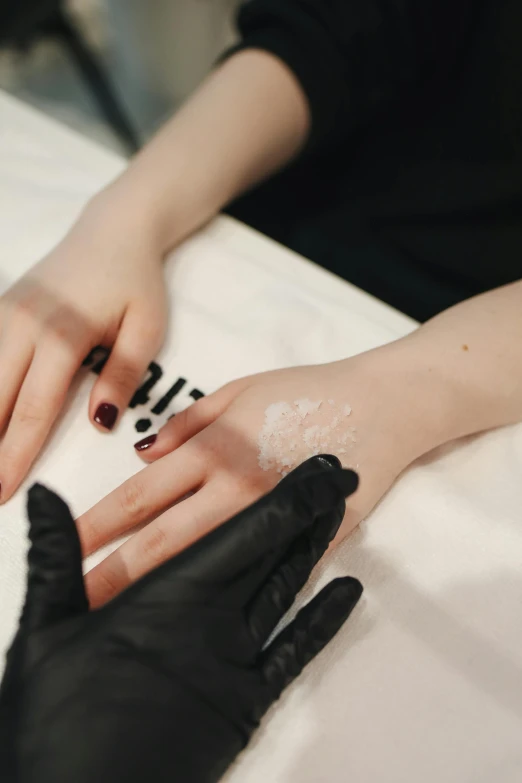 a woman getting her nails done at a salon, a tattoo, by Emma Andijewska, pexels, aestheticism, black leahter gloves, white facepaint, thumbnail, cream