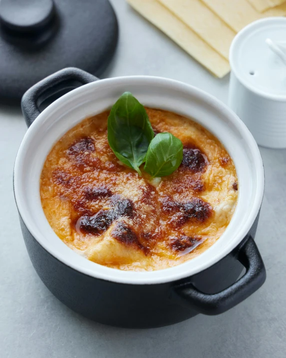 a close up of a pot of food on a table, inspired by Charles Le Roux, unsplash, melted cheese, square, black, flan