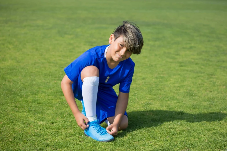 a young boy kneeling on top of a soccer field, by Daniel Schultz, dribble contest winner, kobalt blue, avatar image, laces, ready to model