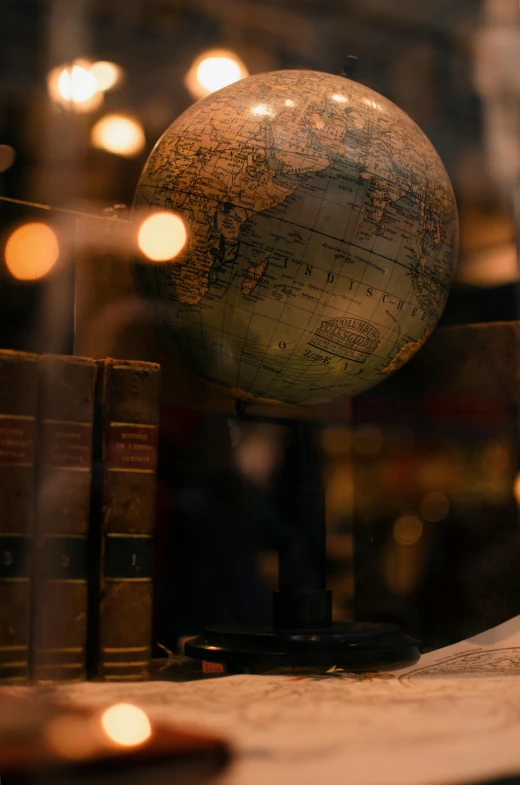 a globe sitting on top of a table next to a pile of books, illuminated features, up close, distant photo