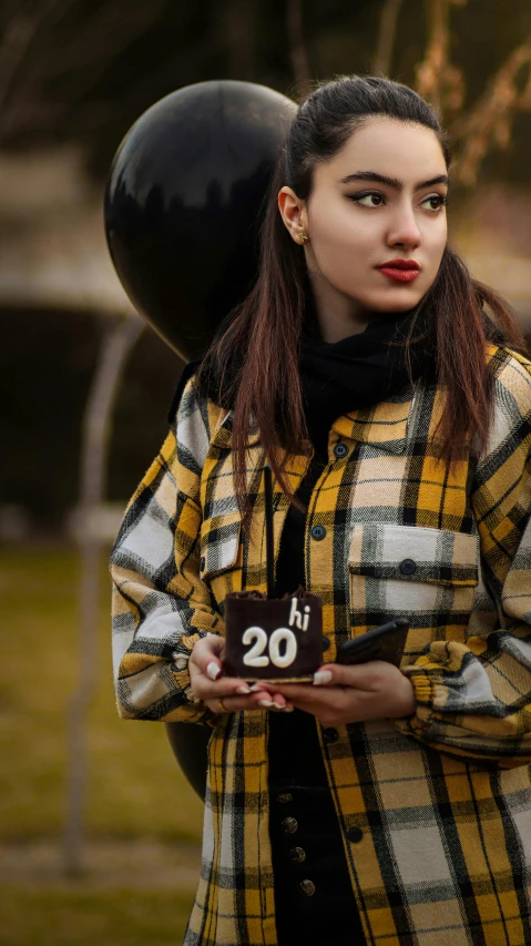 a woman in a plaid coat holding a black balloon, trending on pexels, he is about 20 years old | short, yellow cap, chocolate, celebration