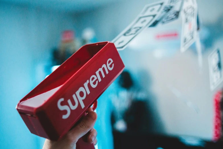 a person holding a red box with the supreme logo on it, a picture, by Robbie Trevino, trending on unsplash, scepter, jr sc maglev, spatula, looking off to the side