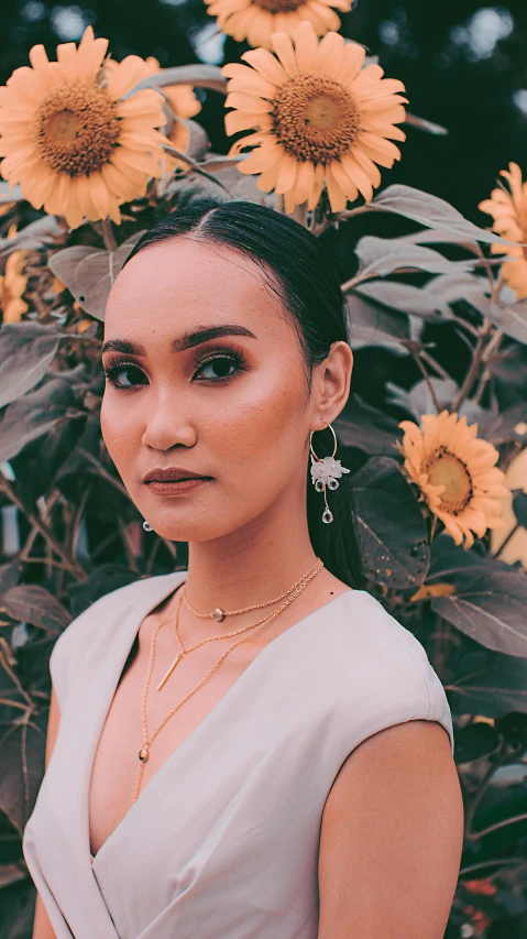 a woman in a white dress standing in front of sunflowers, an album cover, inspired by Ruth Jên, trending on pexels, sumatraism, earrings, portrait image, wearing several pendants, grey