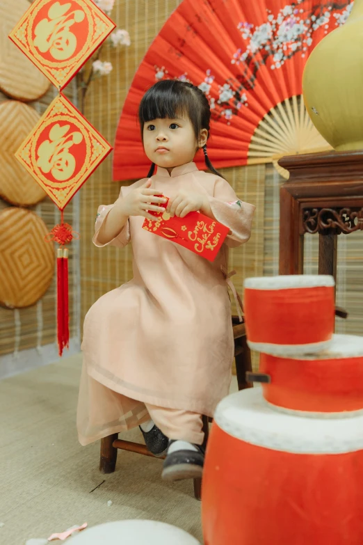 a little girl sitting on a chair holding a red fan, inspired by Ni Duan, pexels contest winner, tea drinking and paper lanterns, brown, square, standing elegantly