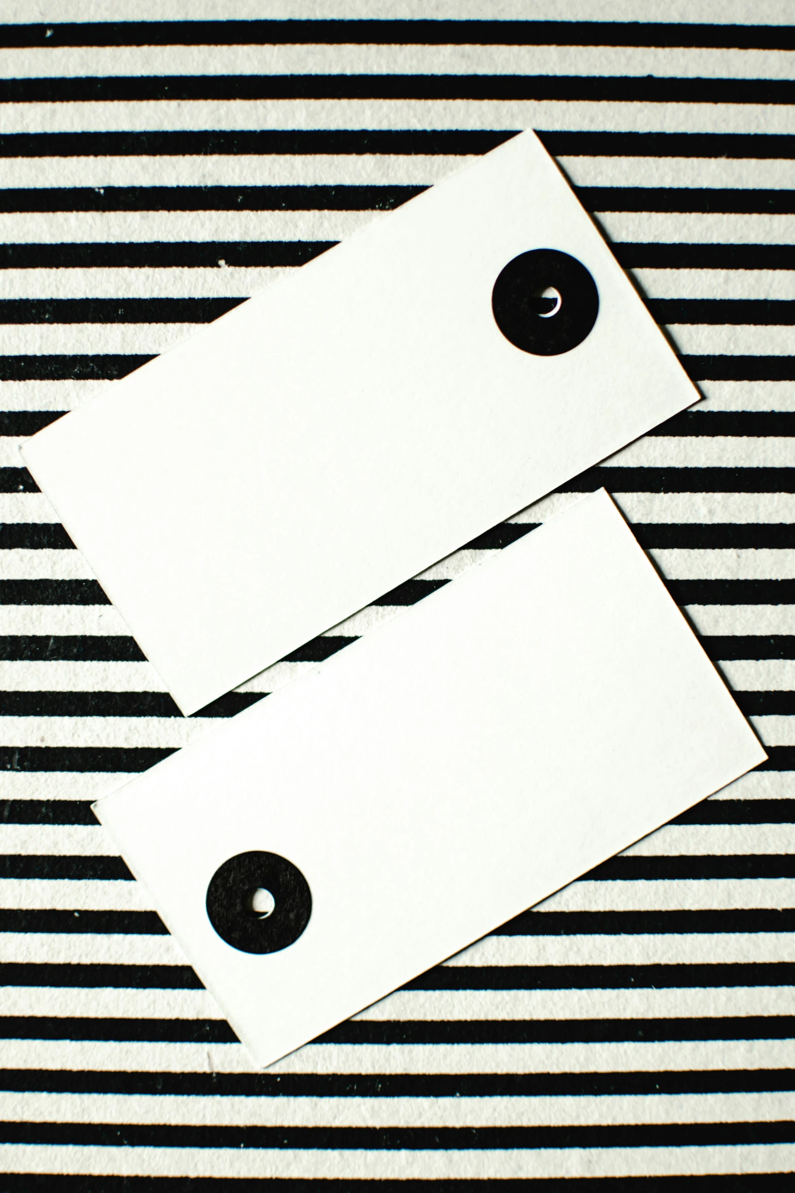 a couple of tags sitting on top of a striped table, inspired by Barnett Newman, unsplash, op art, void eyeballs, blank paper, square black pupil centered, studio quality