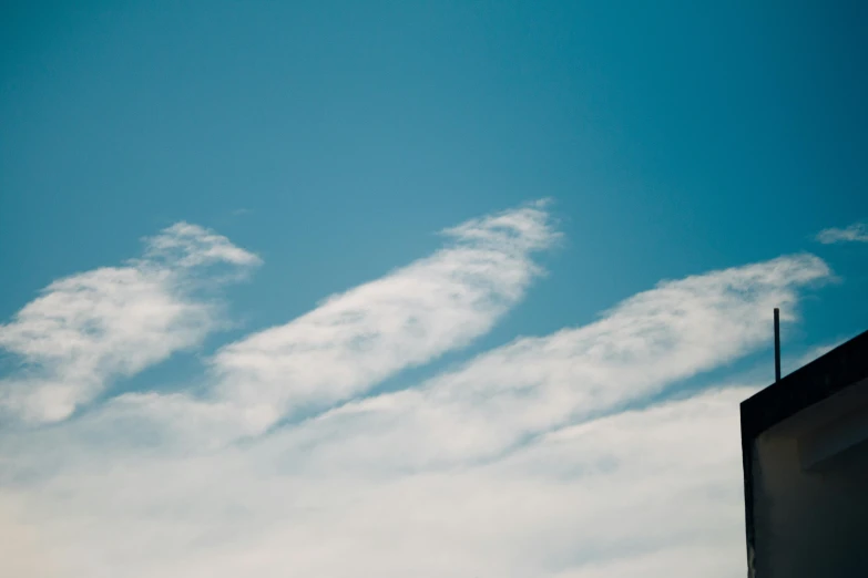 there is a plane that is flying in the sky, by Niko Henrichon, pexels, aestheticism, wispy clouds in a blue sky, 3 layers of sky above each other, close - up photograph, very elongated lines