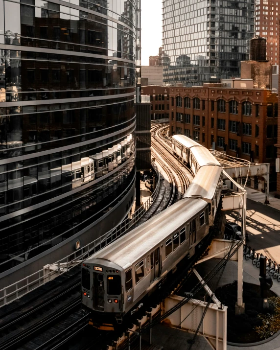 a silver train traveling through a city next to tall buildings, unsplash contest winner, lgbtq, chicago, curved, thumbnail