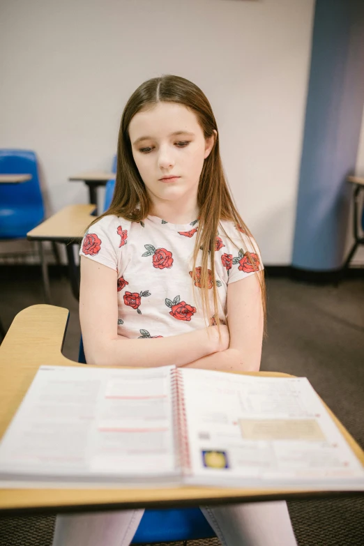 a girl sitting at a desk reading a book, looking confused, standing in class, taken in 2 0 2 0, medium head to shoulder shot