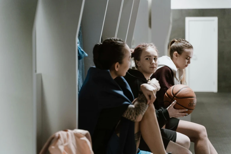 a group of young women sitting next to each other, by Emma Andijewska, trending on pexels, happening, wearing basketball jersey, lockers, juno promotional image, cinematic medium shot